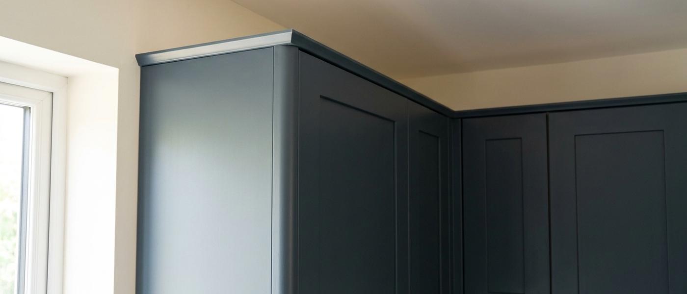 The top corner of a run of dark charcoal painted cabinets with a newly fitted finished end panel and slim top moulding meeting the wall and ceiling